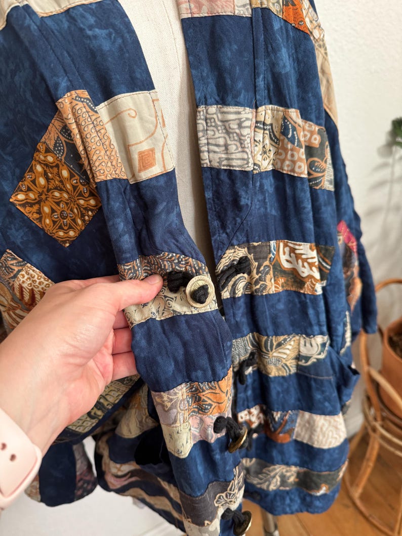 Puede incluir: Chaqueta patchwork en tonos azules, beige y marr&oacute;n. La chaqueta presenta una variedad de cuadrados de tela estampada cosidos. Tiene cierre de botones y un ajuste relajado, adecuado para superponer. El dise&ntilde;o de la chaqueta recuerda a los estilos vintage o bohemios.