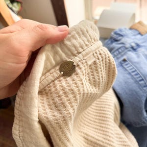 May include: Close-up of a beige waffle-knit fabric with a tag that reads "FP ONE". The fabric is part of a garment, possibly a top or pants, with a textured surface and a soft, light color.