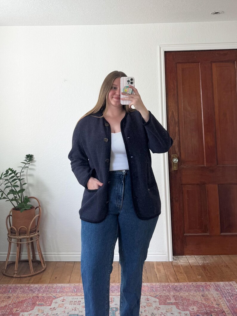 May include: A navy blue button-up jacket with black trim and two front pockets. The jacket is worn over a white vest top and paired with blue jeans. The outfit is casual and suitable for everyday wear.