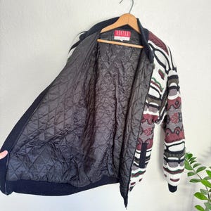 Peut inclure: Une veste en tricot &agrave; motifs noir et blanc avec une fermeture &eacute;clair rouge et une doublure matelass&eacute;e noire. La veste porte une &eacute;tiquette indiquant "Ashton London".