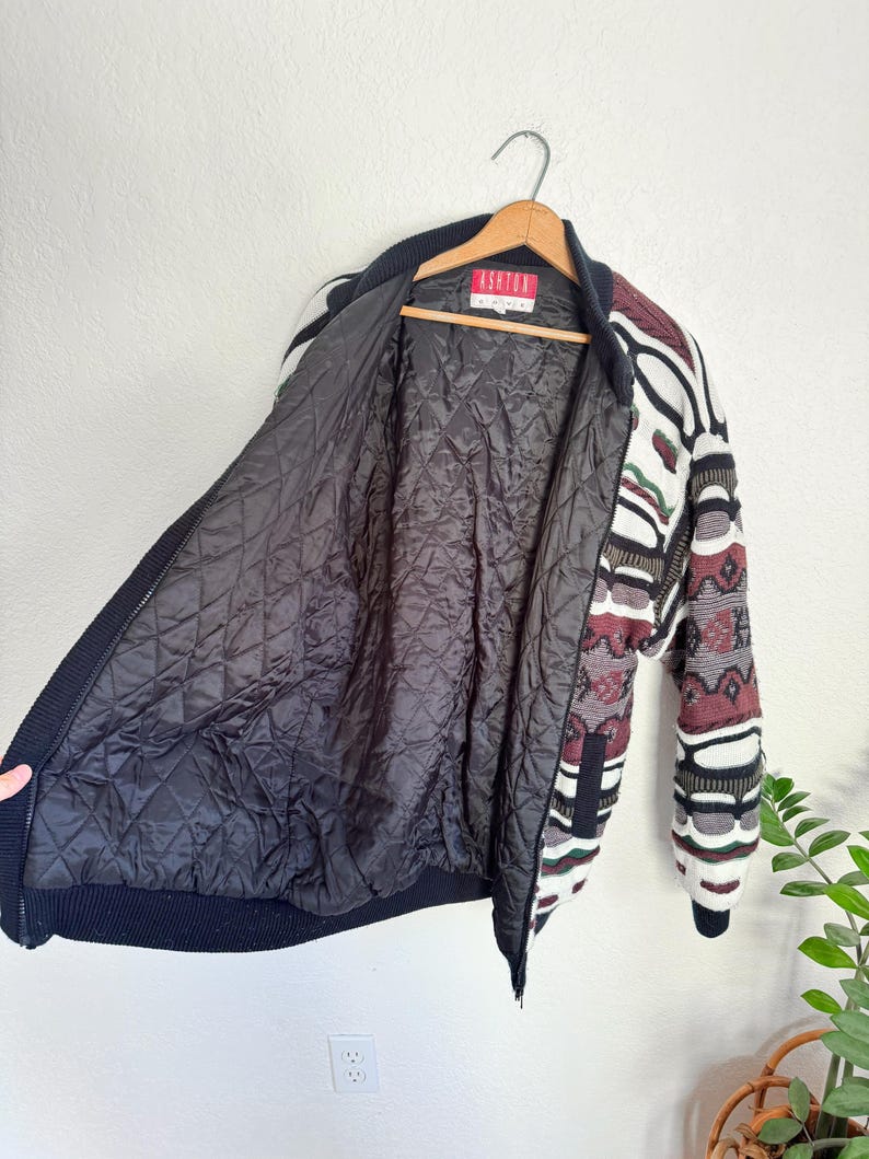Peut inclure: Une veste en tricot &agrave; motifs noir et blanc avec une fermeture &eacute;clair rouge et une doublure matelass&eacute;e noire. La veste porte une &eacute;tiquette indiquant "Ashton London".