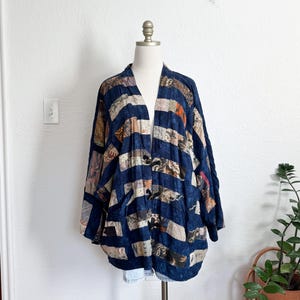 Puede incluir: Una chaqueta azul marino de frente abierto con un dise&ntilde;o de patchwork. La chaqueta presenta rayas horizontales de varias telas estampadas en tonos beige, marr&oacute;n y naranja. La chaqueta se exhibe en un maniqu&iacute;.