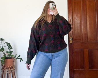 Könnte beinhalten: Ein V-Ausschnitt-Pullover mit einem geometrischen Muster in Grün-, Burgunder- und Blautönen. Der Pullover wird mit hellblauen Jeans kombiniert. Die Ärmel sind lang und die Passform ist locker.