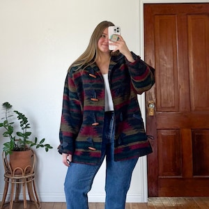 May include: A patterned jacket in shades of navy, burgundy, green, and brown with wooden toggle closures. The jacket is worn with blue jeans. The jacket has a Southwestern-inspired design.