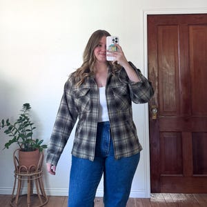 May include: A plaid flannel shirt in shades of brown, black, and tan, with a zipper closure and two chest pockets. The shirt is paired with blue jeans. The outfit is casual and suitable for everyday wear.