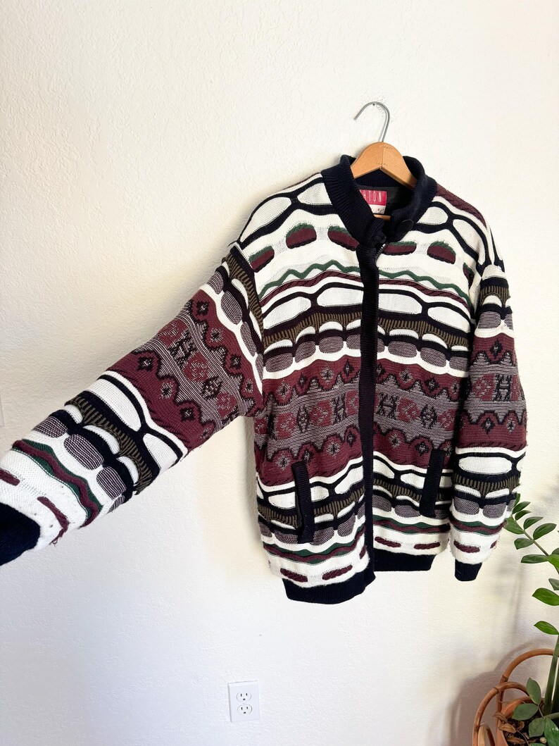 Peut inclure: Un cardigan vintage &agrave; fermeture &eacute;clair avec un motif g&eacute;om&eacute;trique color&eacute; dans les tons de rouge, blanc, noir et vert. Le cardigan a deux poches sur le devant.