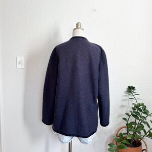 May include: A navy blue long-sleeved jacket with black trim, shown on a mannequin. The jacket has a simple, classic design and is made of a soft material. A versatile piece of clothing.