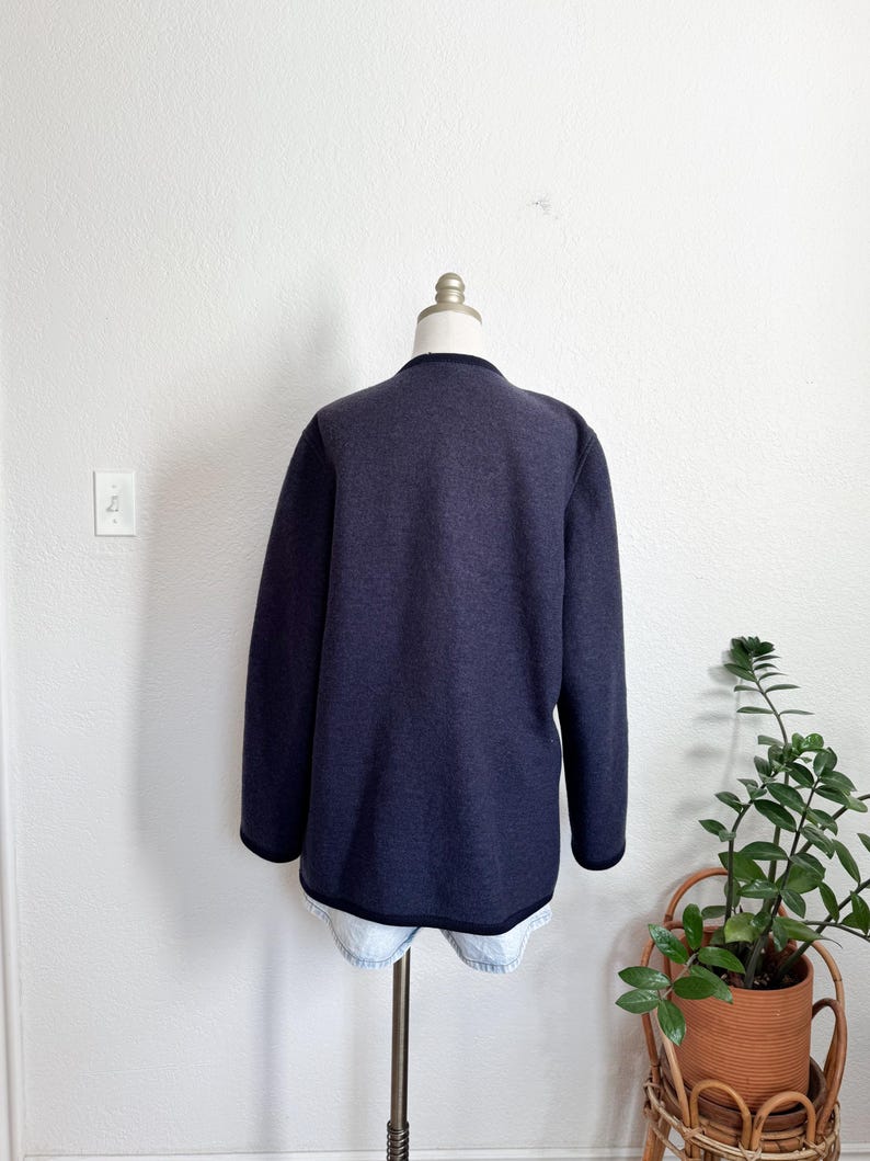 May include: A navy blue long-sleeved jacket with black trim, shown on a mannequin. The jacket has a simple, classic design and is made of a soft material. A versatile piece of clothing.