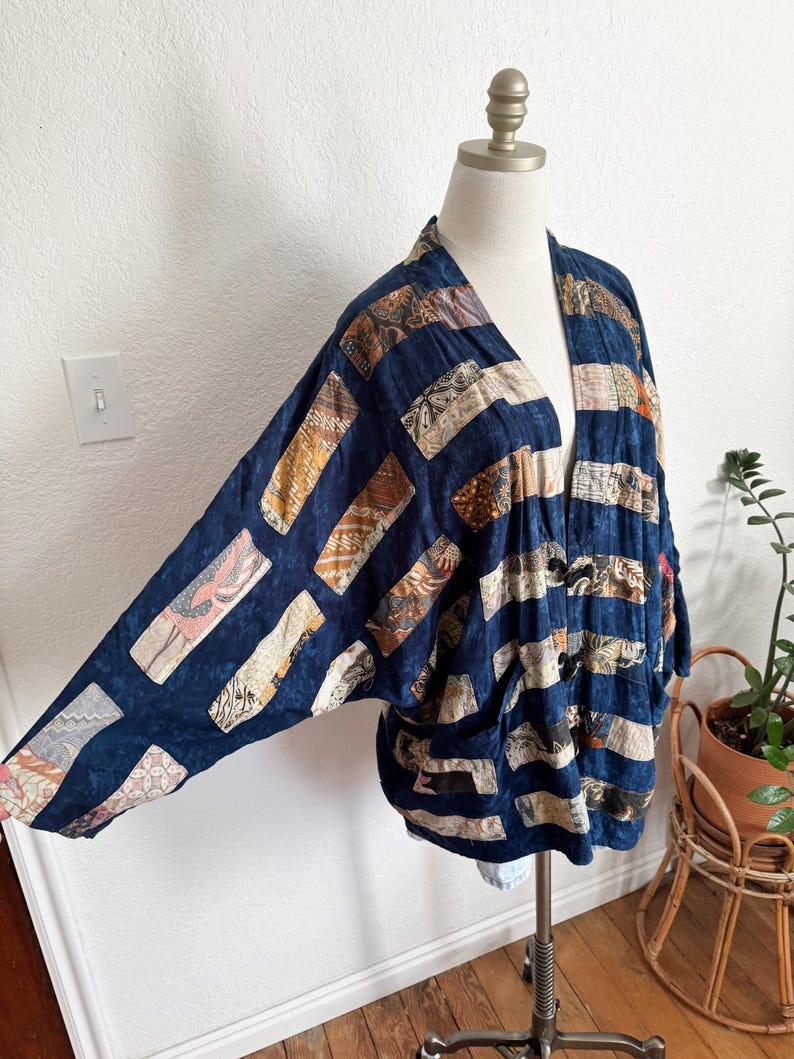Puede incluir: Chaqueta estilo kimono azul marino con dise&ntilde;o patchwork. La chaqueta presenta parches rectangulares en varios colores y patrones, incluyendo beige, marr&oacute;n y rosa. La prenda se exhibe en un maniqu&iacute;, mostrando su ajuste holgado y frente abierto.