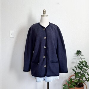May include: A navy blue button-down jacket with black trim and silver-coloured buttons. The jacket has two front pockets and is displayed on a mannequin. The jacket is paired with denim shorts.