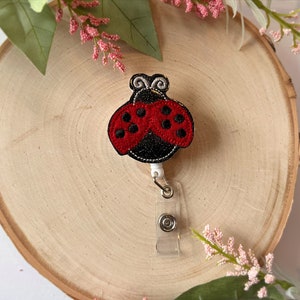 May include: A red and black ladybug with white accents is attached to a retractable badge holder. The badge holder is clear plastic with a silver clip.
