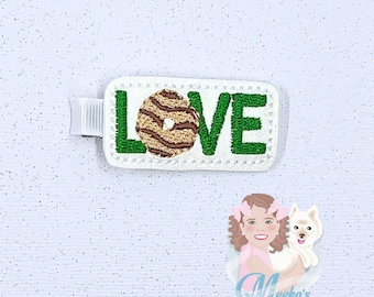 May include: A white rectangle with green letters spelling "LOVE" and a brown and white donut in the middle. The rectangle is on a white glittery background.