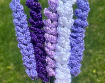 May include: A bouquet of six crocheted lavender flowers in shades of purple, lavender, and white. The flowers are made with yarn and have a realistic appearance.