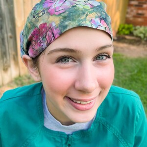 May include: A woman wearing a green scrub top with a floral print surgical cap. She is smiling and looking at the camera.