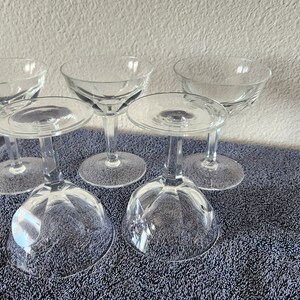 May include: Set of six clear glass champagne coupes with a fluted design. The coupes are arranged in a group on a blue towel.