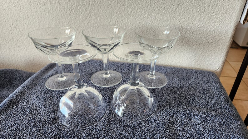 May include: Set of six clear glass champagne coupes with a fluted design. The coupes are arranged in a group on a blue towel.