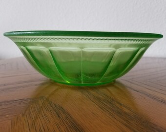 May include: A vintage green glass bowl with a fluted design. The bowl is made of Depression glass and has a slightly frosted finish.