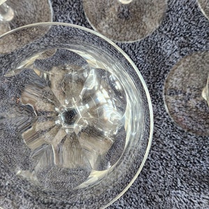 May include: Close-up of the bottom of a clear glass goblet with a cut-glass design. The goblet is sitting on a gray textured surface.