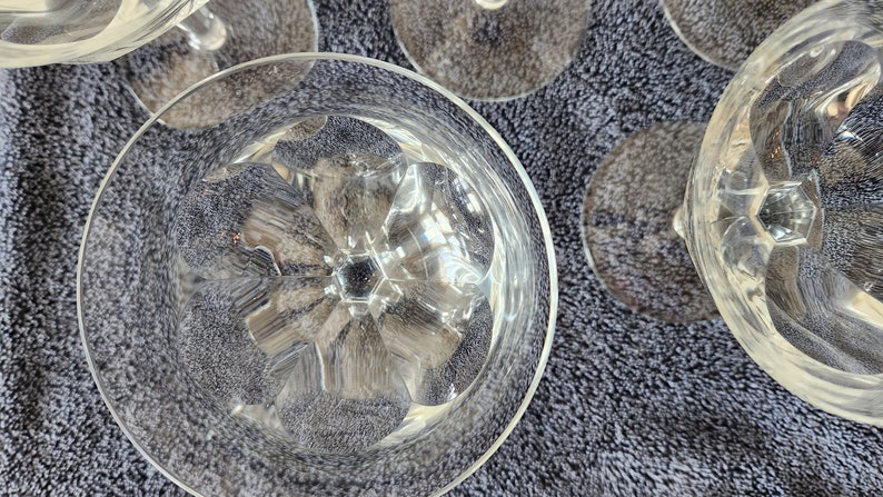 May include: Close-up of the bottom of a clear glass goblet with a cut-glass design. The goblet is sitting on a gray textured surface.