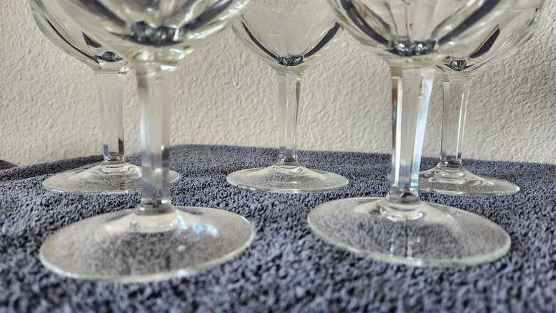 May include: Four clear glass wine glasses with a diamond pattern on the bowl and a long, thin stem. The glasses are sitting on a gray, textured surface.