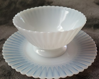 May include: A white opalescent glass bowl with a scalloped edge sits on a matching saucer. Both pieces have a delicate, fluted design.