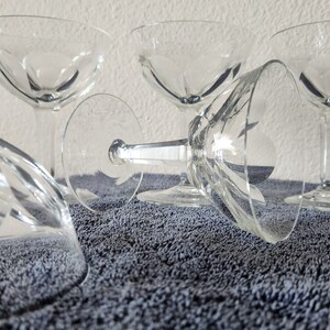 May include: Four clear glass champagne coupes with a cut glass design. The glasses are arranged on a gray textured surface.