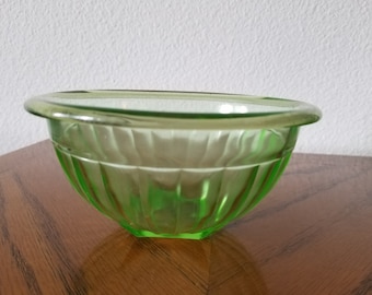 May include: A green glass bowl with a fluted design. The bowl is made of Depression glass and has a vintage look.