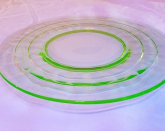 May include: A set of three clear glass plates with a green rim. The plates are stacked on top of each other.