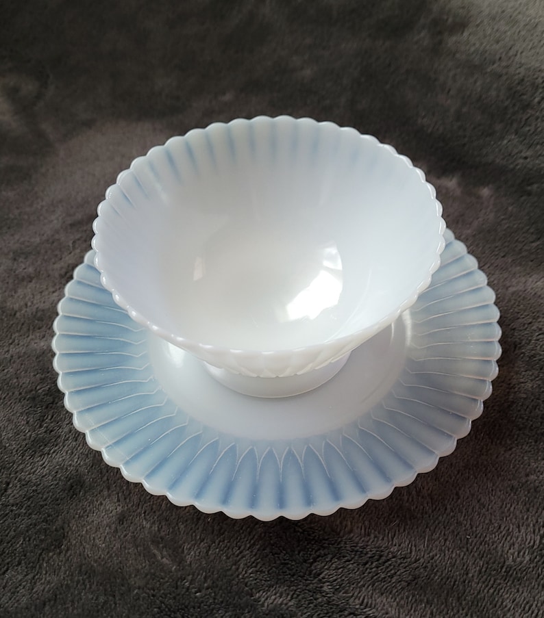 Pu&ograve; includere: Una ciotola in vetro di latte bianco con un bordo a festoni e un piatto abbinato. La ciotola e il piatto hanno una glassa blu iridescente.