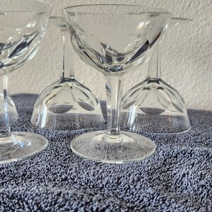 May include: Set of six clear glass stemmed cocktail glasses with a cut glass design. The glasses are arranged in a row on a gray textured surface.