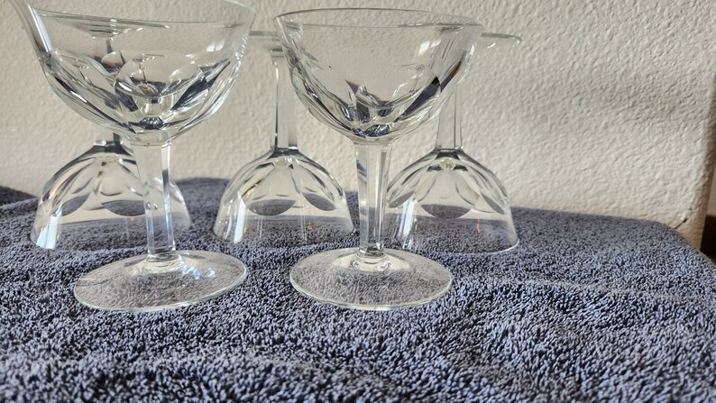 May include: Set of six clear glass stemmed cocktail glasses with a cut glass design. The glasses are arranged in a row on a gray textured surface.