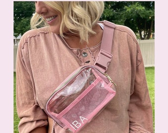 May include: A clear pink belt bag with a mesh design and gold accents. The bag has the initials "IBA" embroidered on the front. The bag is stadium approved and more colors are available.