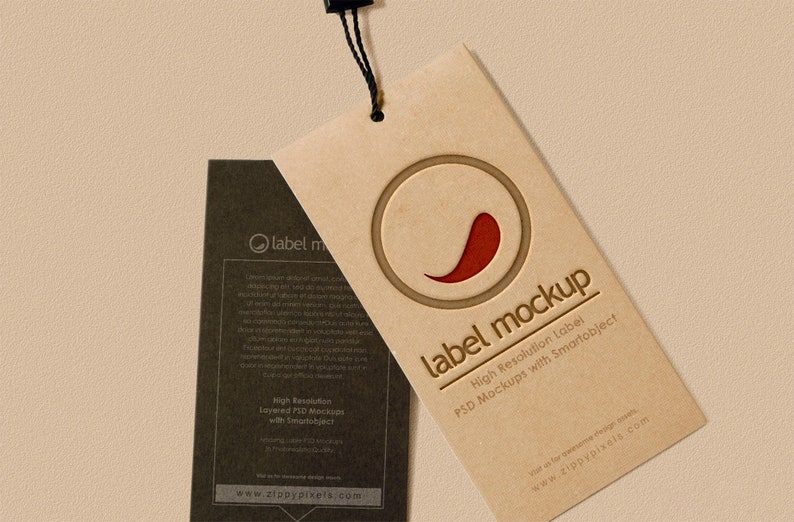 May include: A brown paper label mockup featuring a red chilli pepper graphic and the text "label mockup" in a white font. The text below the graphic reads "High Resolution Label PSD Mockups with Smartobject". The website address "www.zippypixels.com" is printed at the bottom of the label.