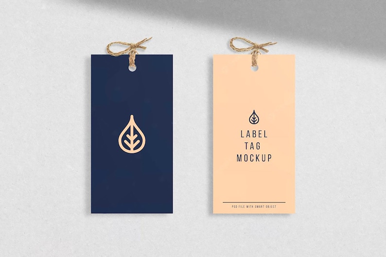 May include: Two blank label tags with a string and a hole for hanging. The tag on the left is navy blue with a leaf design. The tag on the right is peach with the text "LABEL TAG MOCKUP".