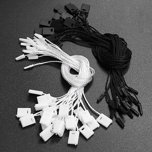 May include: A close-up of a set of white and black string tags with plastic tips. The tags are bundled together and ready to be used for labelling or attaching to items.