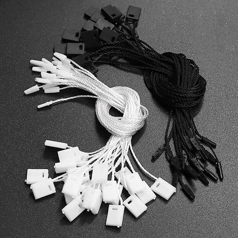 May include: A close-up of a set of white and black string tags with plastic tips. The tags are bundled together and ready to be used for labelling or attaching to items.