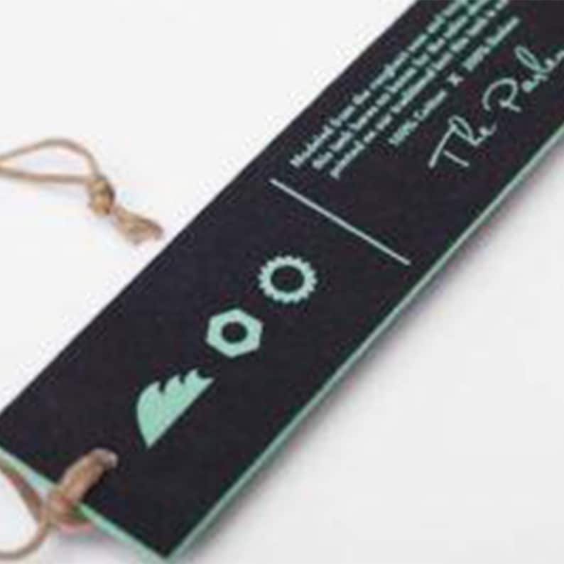 May include: Black and white tag with a green logo featuring a stylized gear and bolt. The text "The Pale" is written in white on the tag.