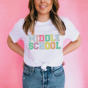 May include: White t-shirt with the text "MIDDLE SCHOOL" in colorful, glittery letters.
