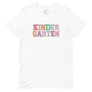 May include: White t-shirt with the word "KINDERGARTEN" in colorful, glittery letters.