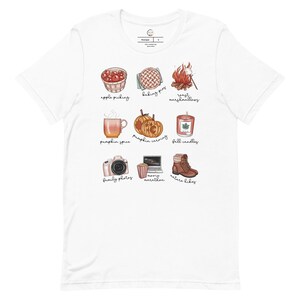 May include: White t-shirt with a graphic design of nine fall-themed icons. The icons include apple picking, baking pies, roasting marshmallows, pumpkin spice, pumpkin carving, fall candles, family photos, movie marathon, and nature hikes.