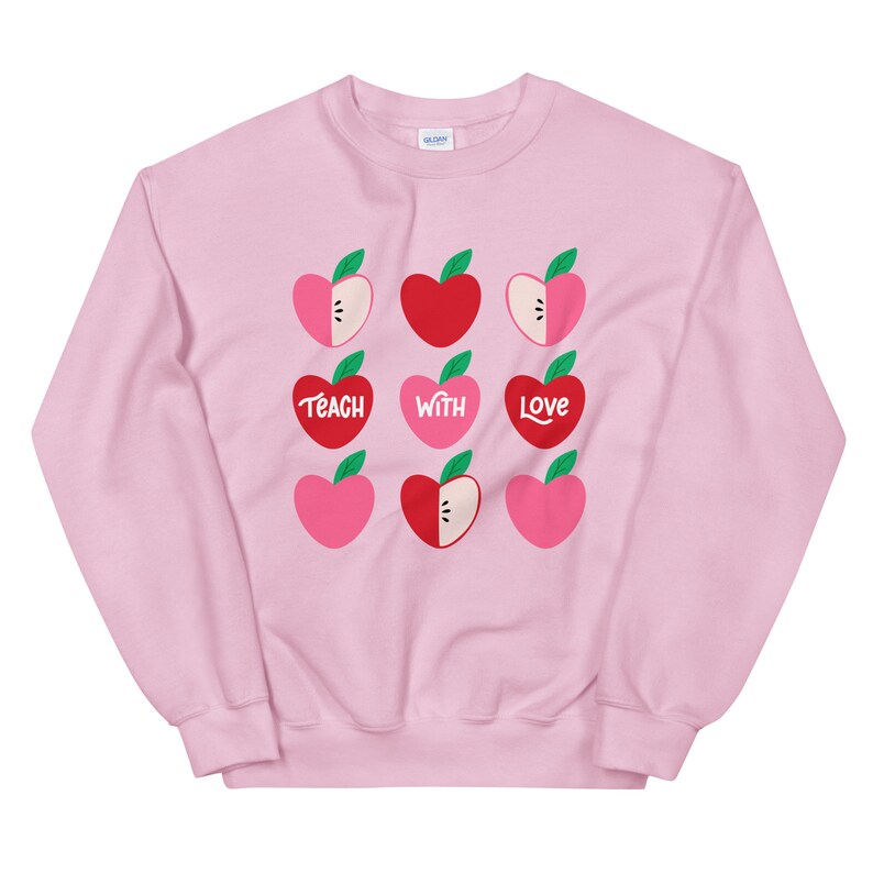 Puede incluir: Sudadera rosa con un gr&aacute;fico de manzanas rojas y rosas y el texto "Teach with Love".