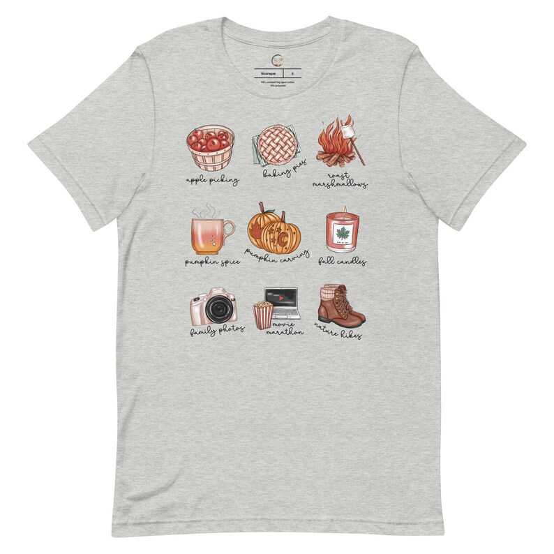 May include: A gray t-shirt with a white design of fall activities. The design includes illustrations of apple picking, baking pies, roasting marshmallows, pumpkin spice, pumpkin carving, fall candles, family photos, movie marathon, and nature hikes.