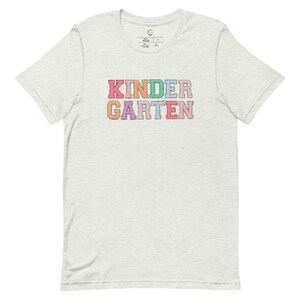 May include: A light grey t-shirt with the word "KINDERGARTEN" printed in colorful letters. Each letter is a different color, including pink, purple, blue, green, and orange.