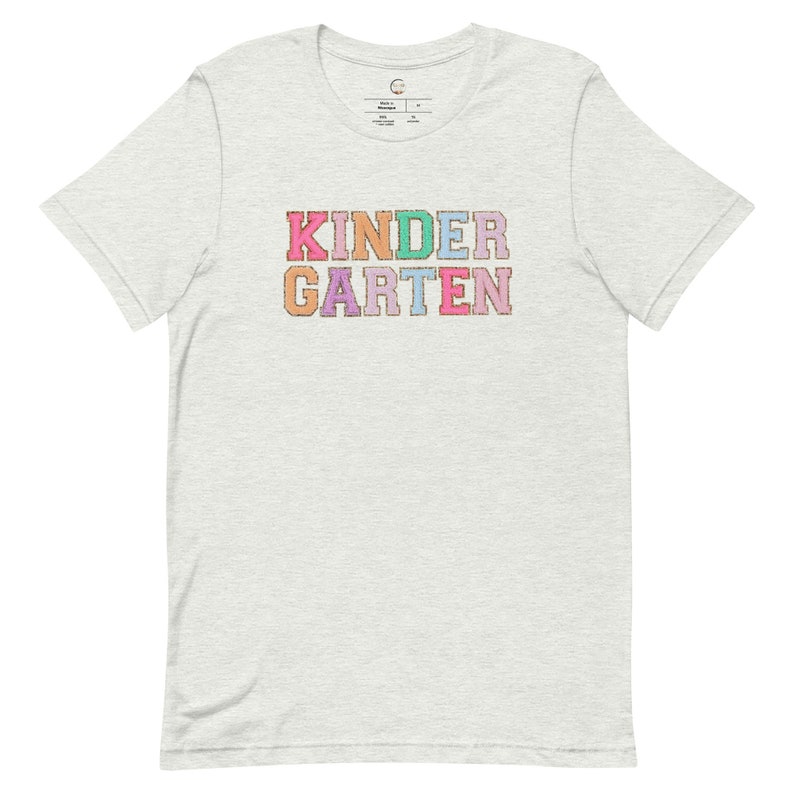 May include: A light grey t-shirt with the word "KINDERGARTEN" printed in colorful letters. Each letter is a different color, including pink, purple, blue, green, and orange.