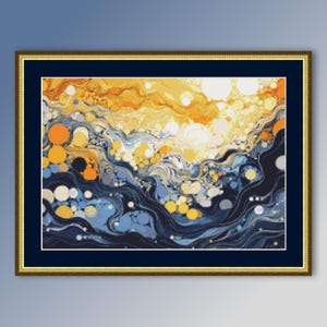 以下が含まれることがあります： 金色のフレームに入った抽象的なクロスステッチアート。黄色、オレンジ、青、白を使い、波のような流れるようなデザインです。作品は、濃い青色のマットが付いた金色のフレームに額装されています。