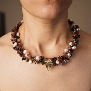 May include: A multi-strand necklace with brown, pink, and white beads, and a gold leaf pendant.