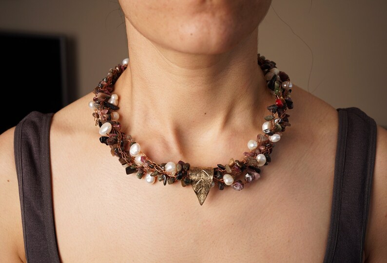 May include: A multi-strand necklace with brown, pink, and white beads, and a gold leaf pendant.