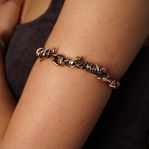 May include: A copper and brass arm cuff with a twisted wire design and a small decorative element.