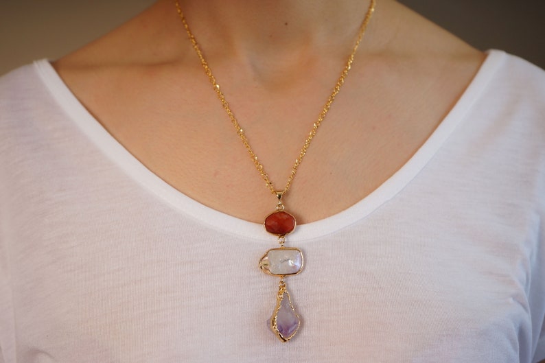 May include: A gold chain necklace with a pendant featuring three stones: a red carnelian, a white pearl, and a purple amethyst.