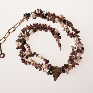May include: A multi-strand necklace made with copper wire, small pink and green stones, and white pearls. The necklace has a leaf-shaped pendant and a brass clasp.